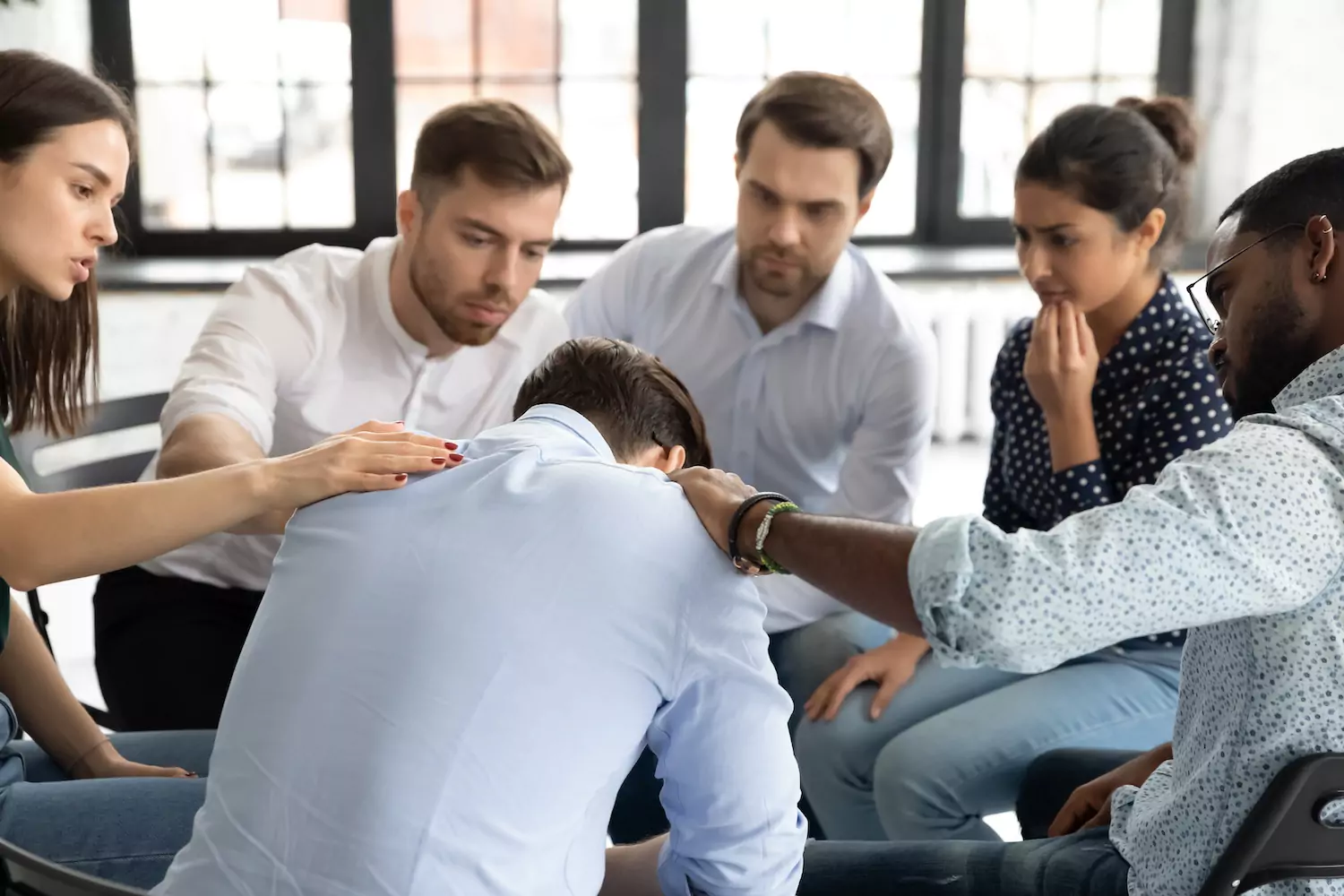 A photo of a prayer group laying their hands on a grieving person.