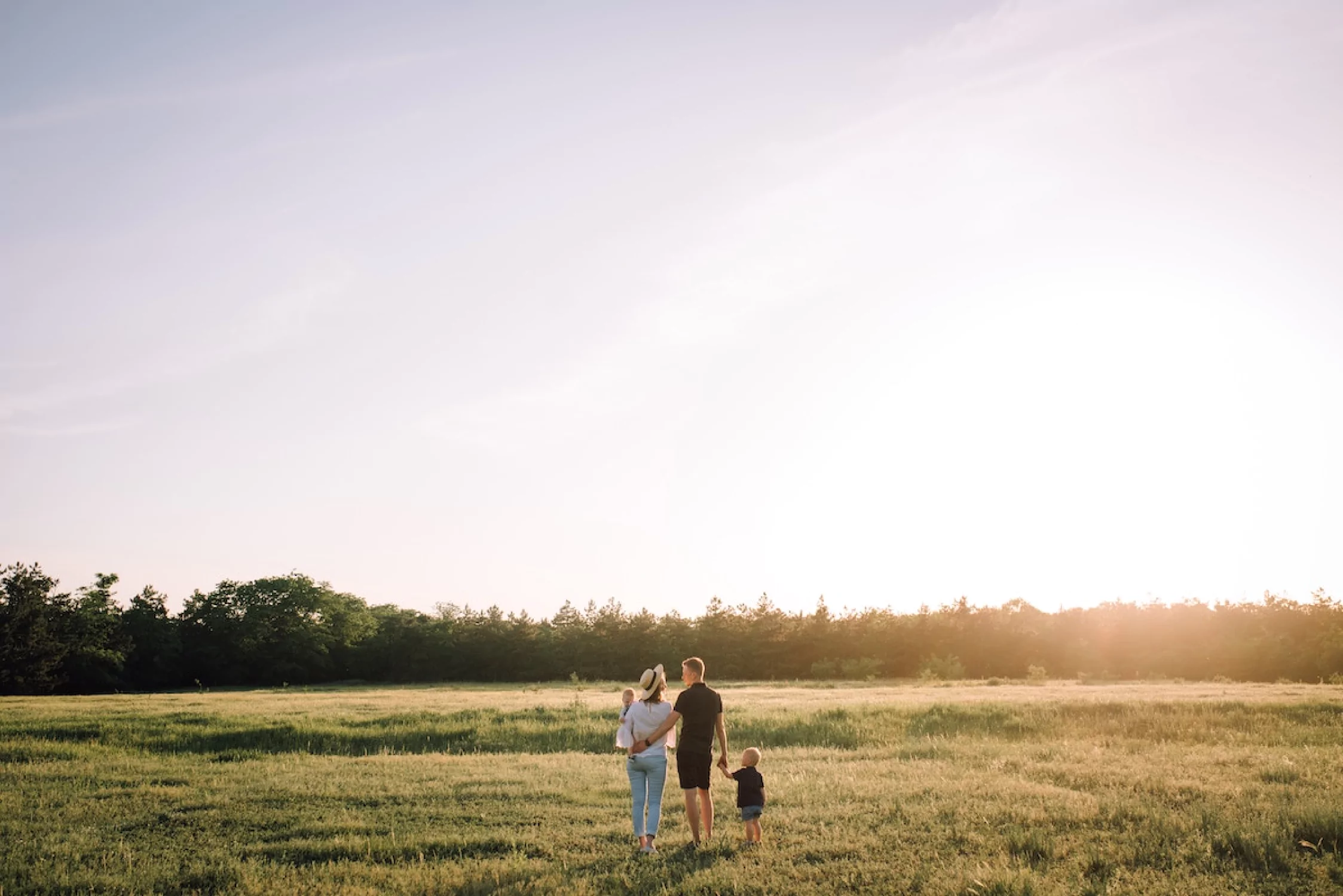a family walking together in a field, the mom holding a baby and the dad holding a child's. hand