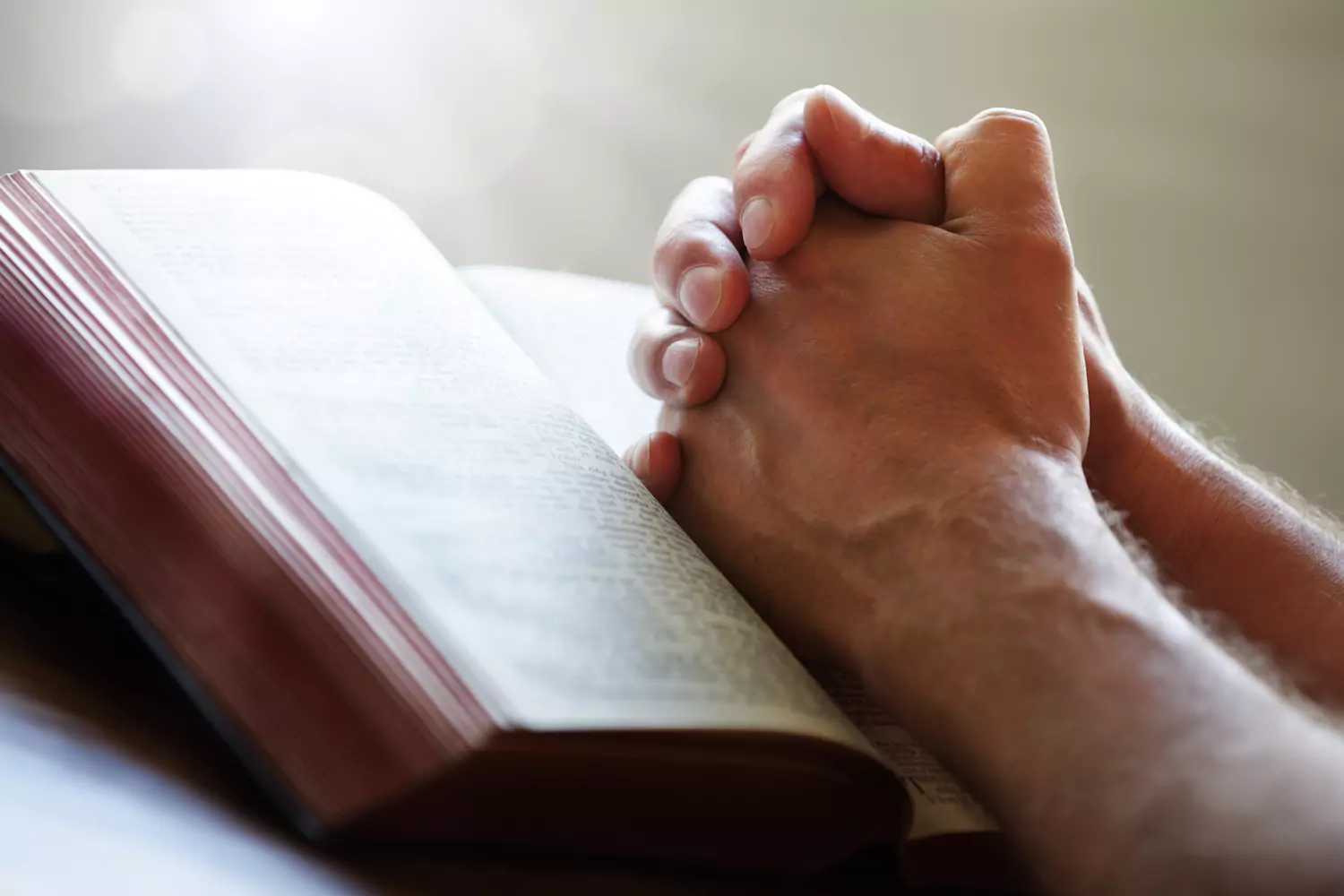 A pair of hands folded in prayer resting on a Bible.