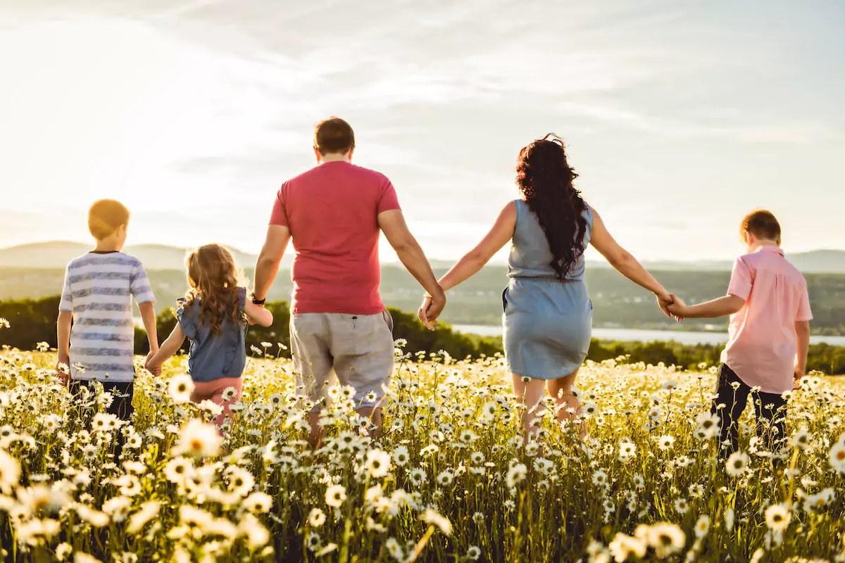 Family of 5 holding hands walking through a field of daisies