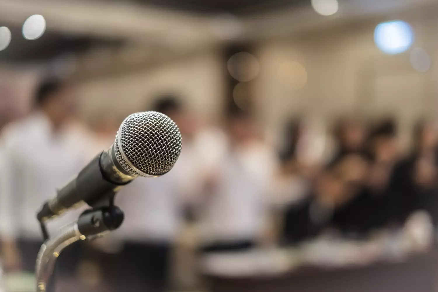 A photo of a microphone in front of an assembly. The photo of the microphone is sharp and in-focus, while the assembly in the background is blurred and softly focused.