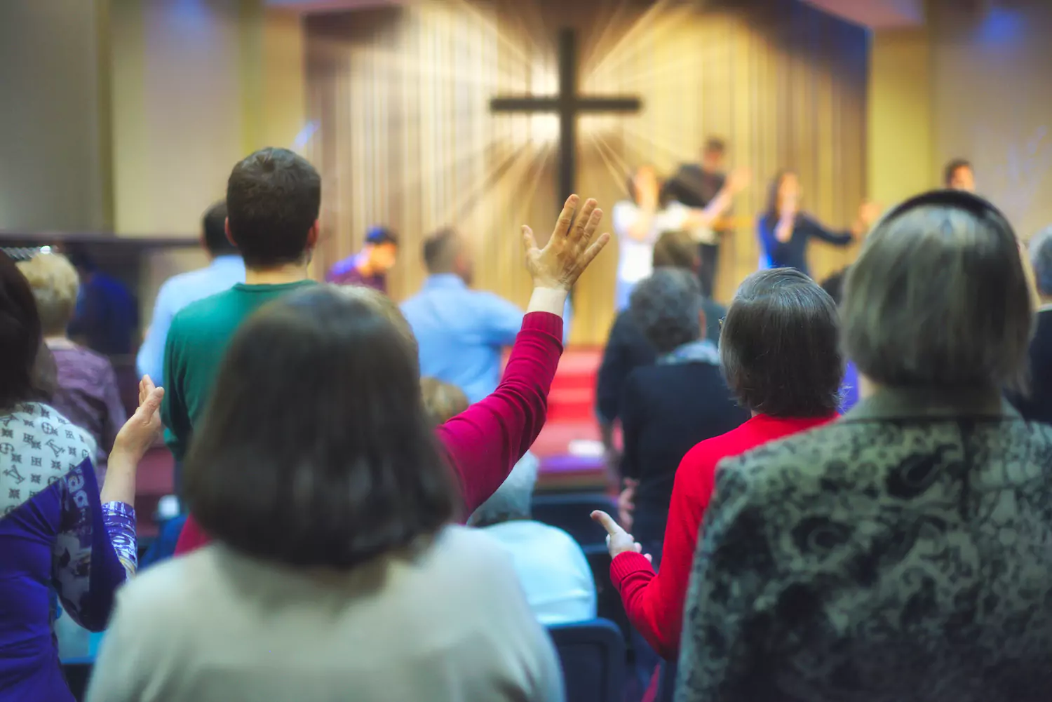A group of people in a protestant church worshipping, some with their hands in the air at the foot of a cross.