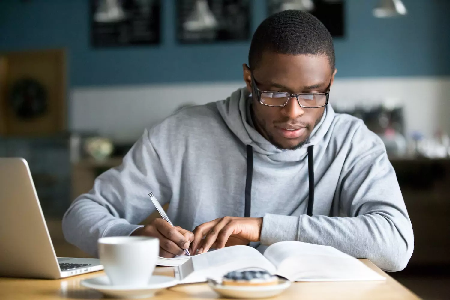 Photo of a studious young man with his computer open, and he's taking notes to sharpen his knowledge and leadership skills.