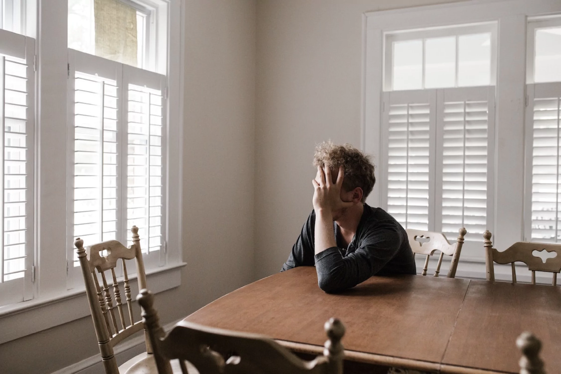 A man sits at a kitchen table, his head in his hands, suffering from grief. Here is an example of how you, as a pastor, can pray for those who grieve following the tragic loss of a suicide.