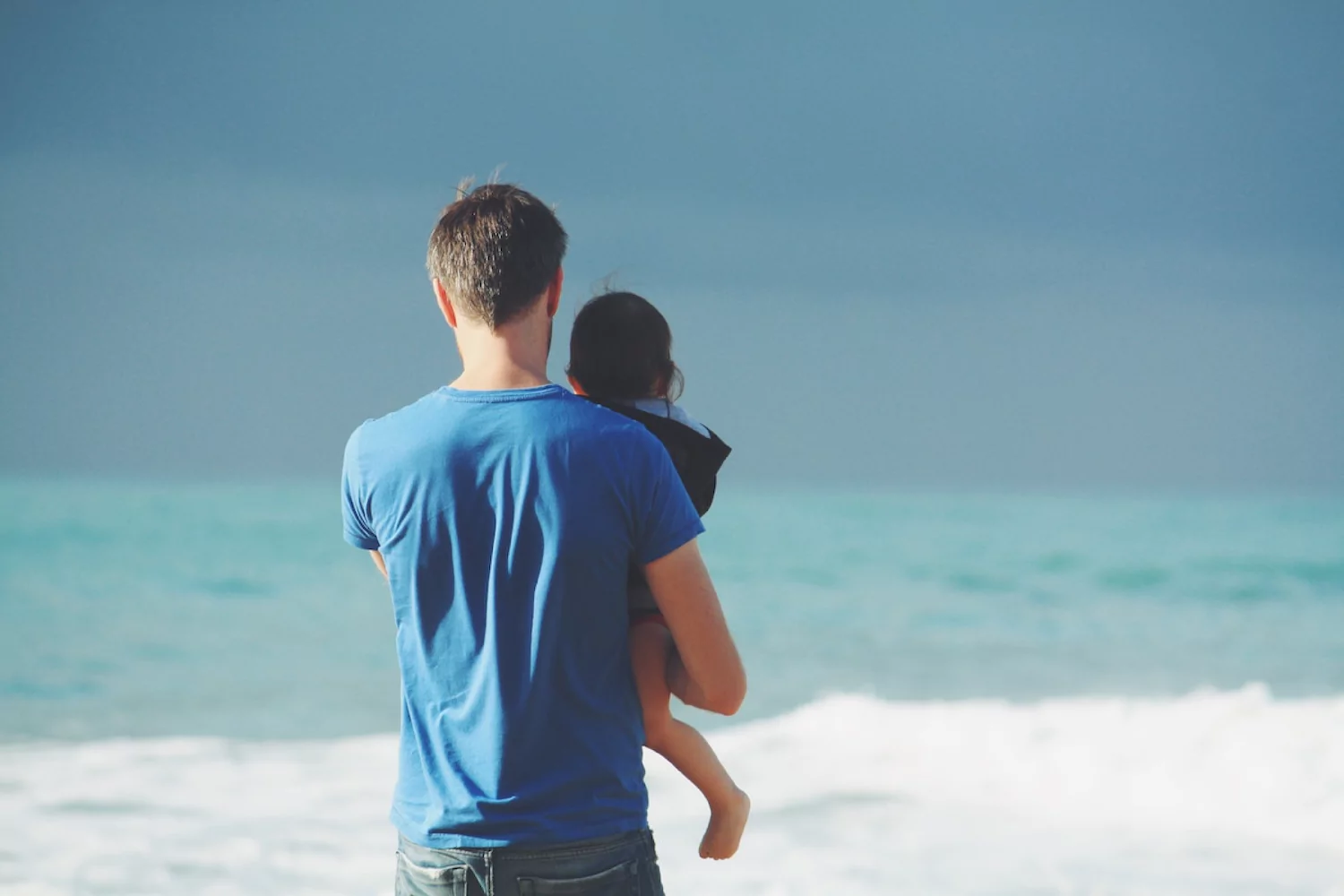 a pastor holding his young daughter as they look at the ocean together