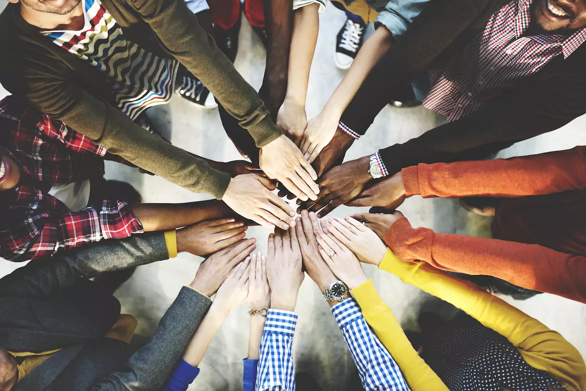 People of different colors standing in a circle and putting their hands in the middle