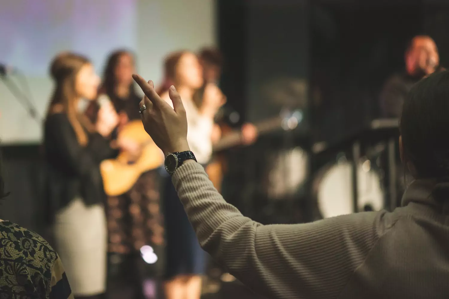 a church member raises their hand in worship as the worship team plays on stage