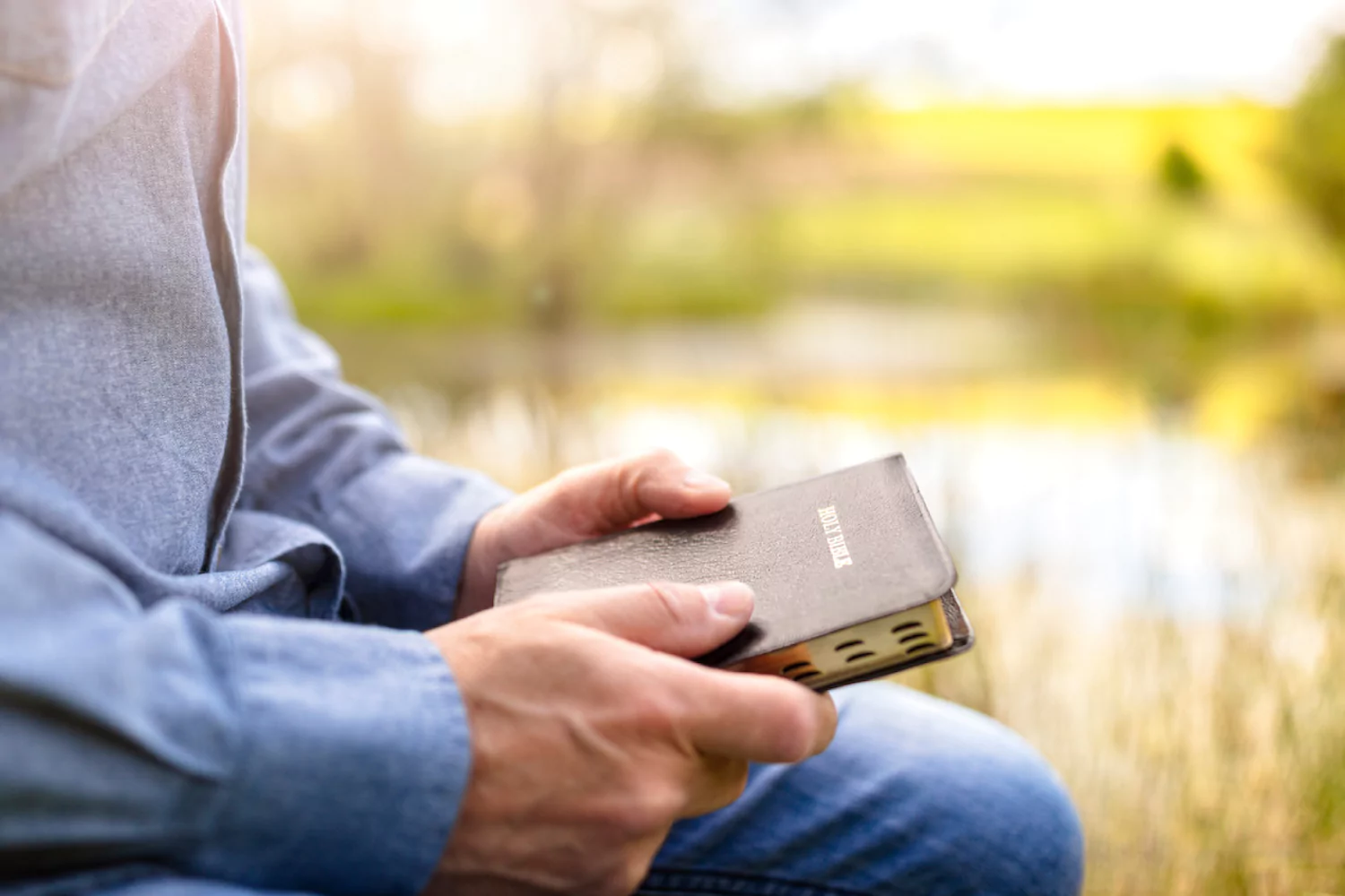 a pastor sits outside by a pond, holding a Bible and considering his calling
