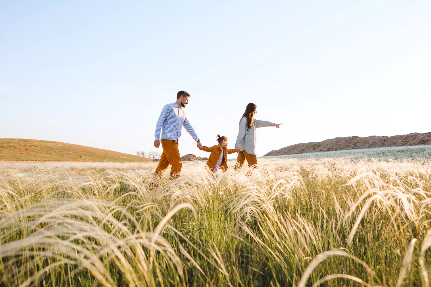 a pastor in his wife hold their child's hand and walk through a field of tall grass