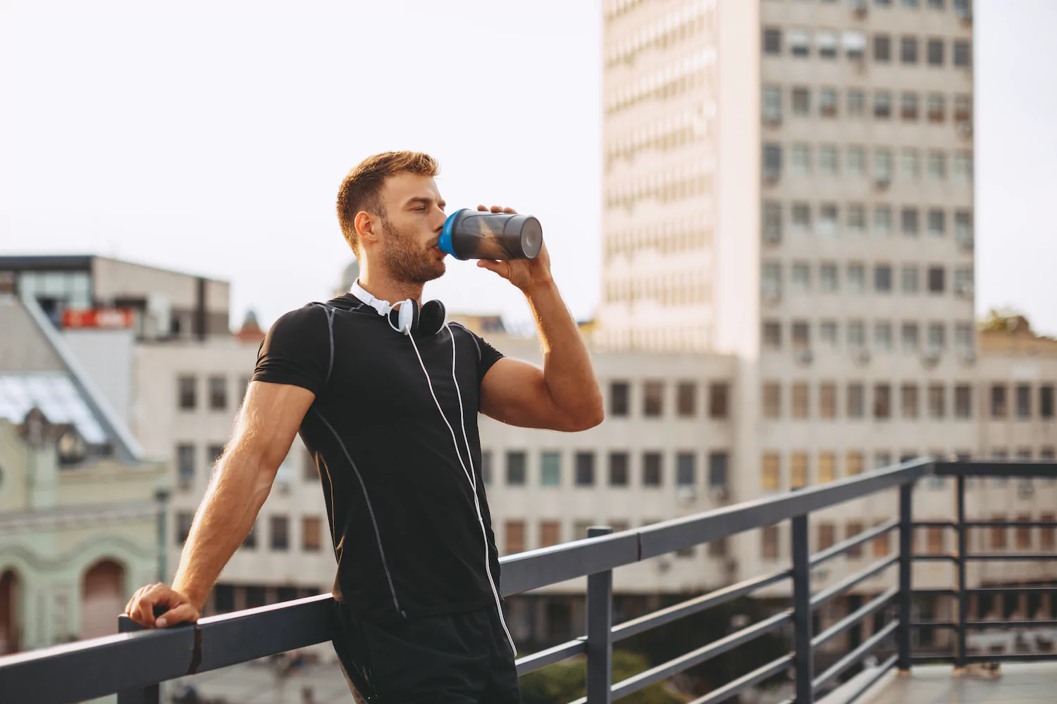 A man rests on a rail drinking a protein shake following a workout, symbolizing spiritual discipline.