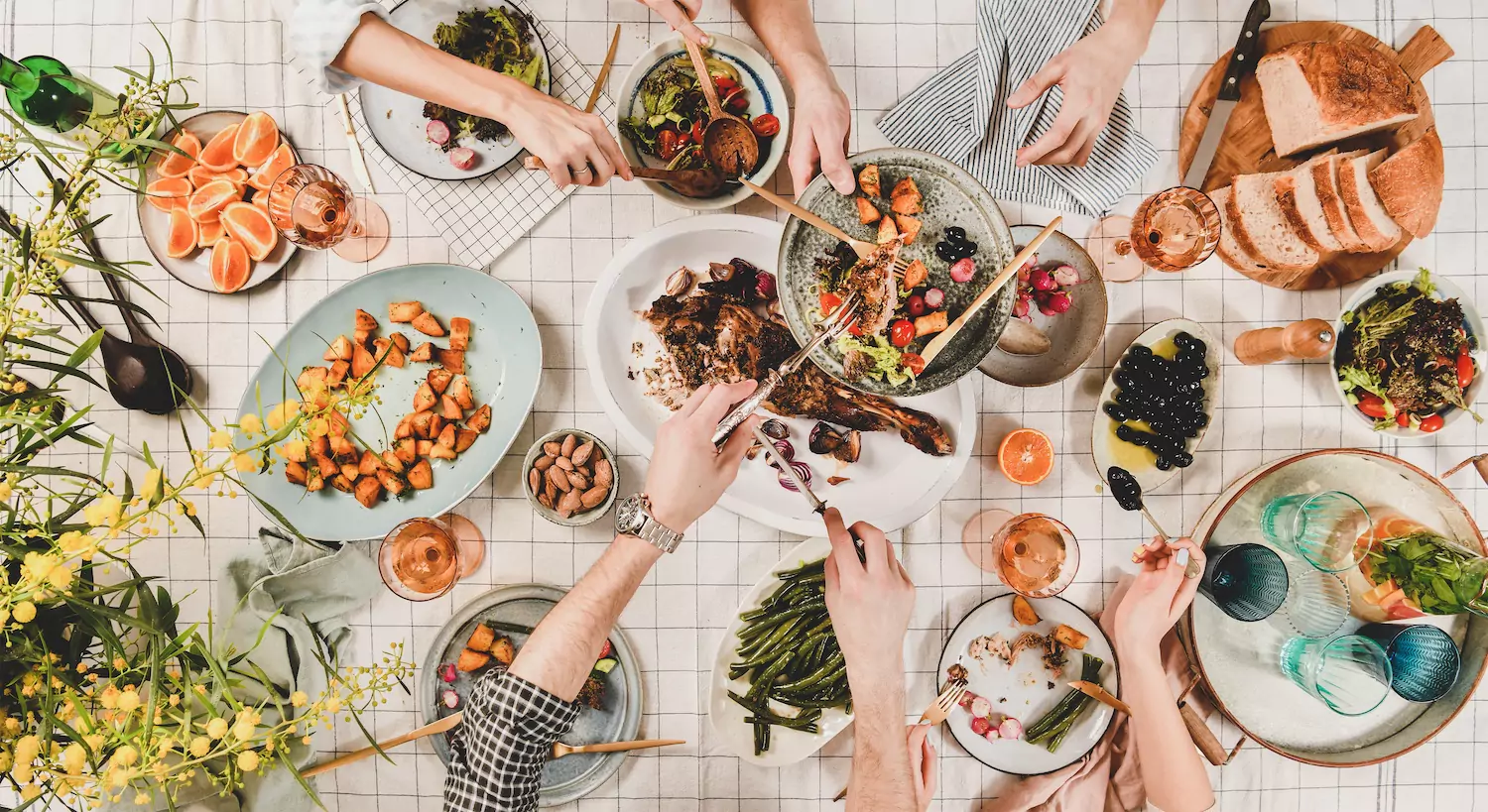 Overhead shot of a table laden with colorful food and hands reaching to fill their plates in celebration of Easter.