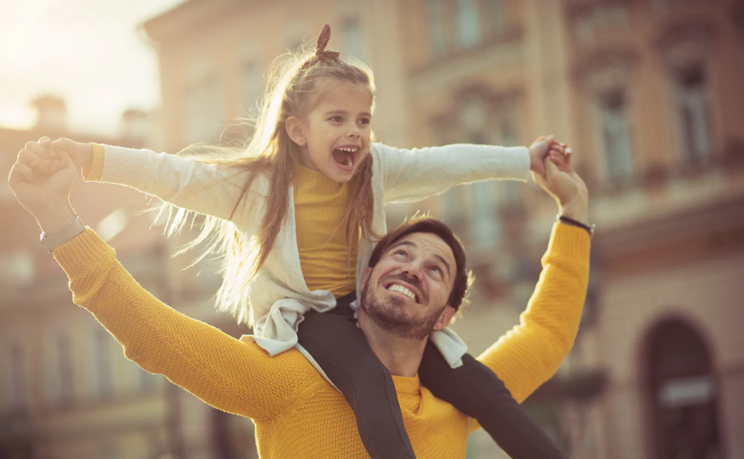 A pastor dad in a yellow shirt walks with his little girl on his shoulders.