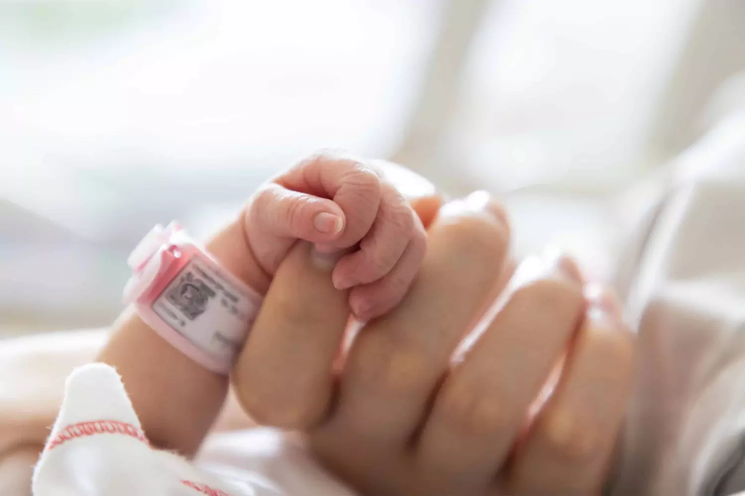 A mother holds the hand of her newborn baby.