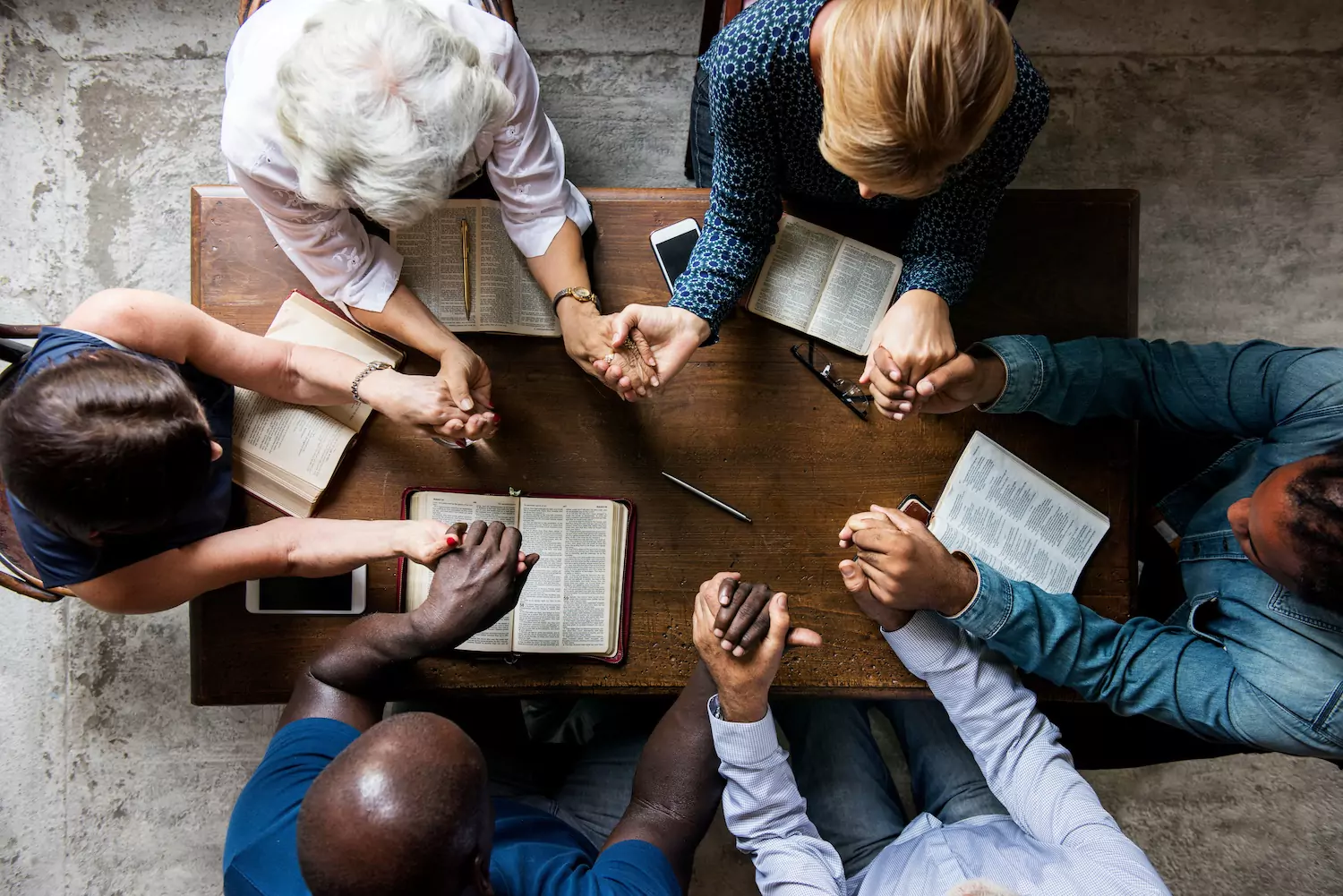 A group of church members sit around a coffee table, holding hands to pray the Psalms.