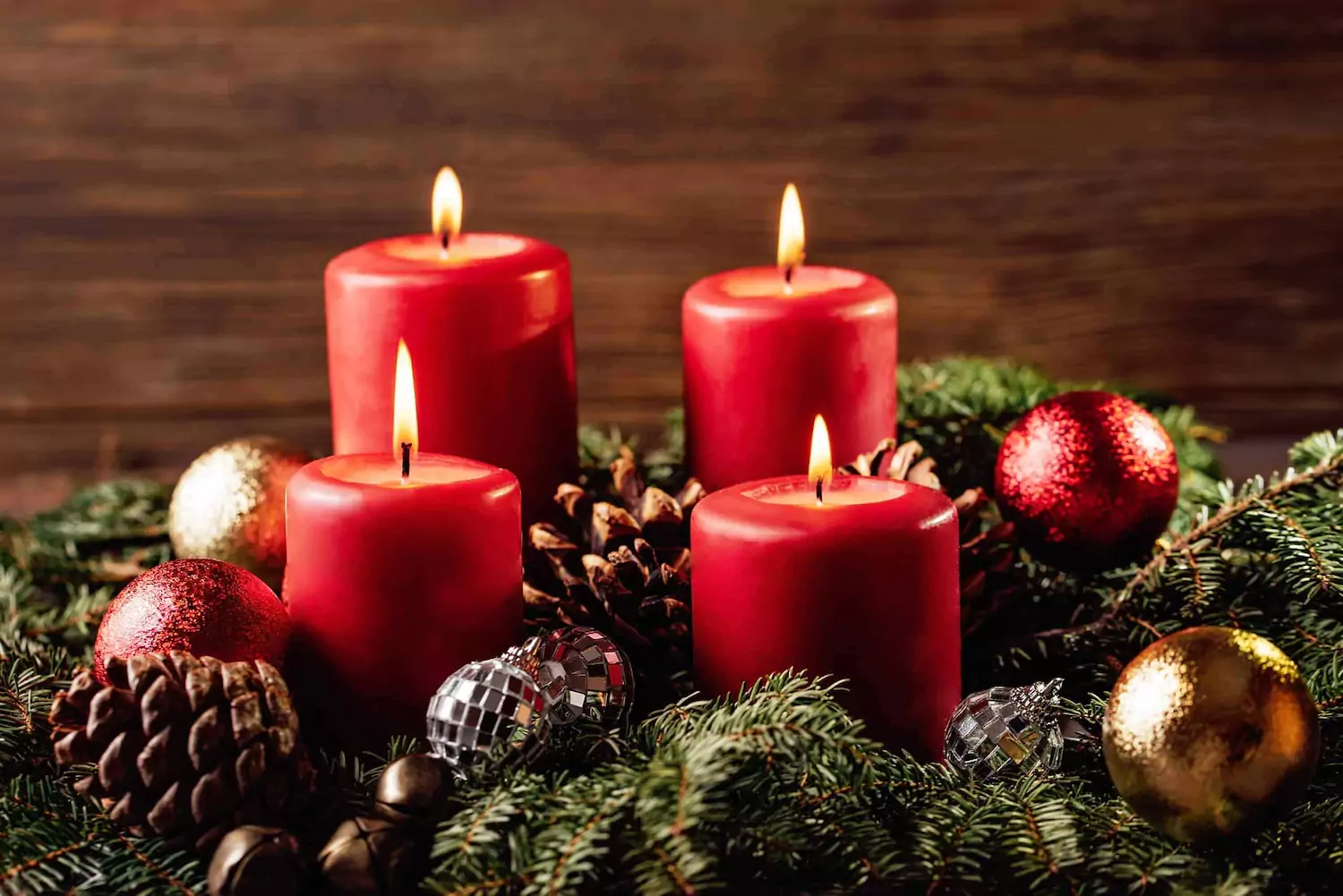 Red candles arranged in Christmas greenery containing pine cones and ornaments.