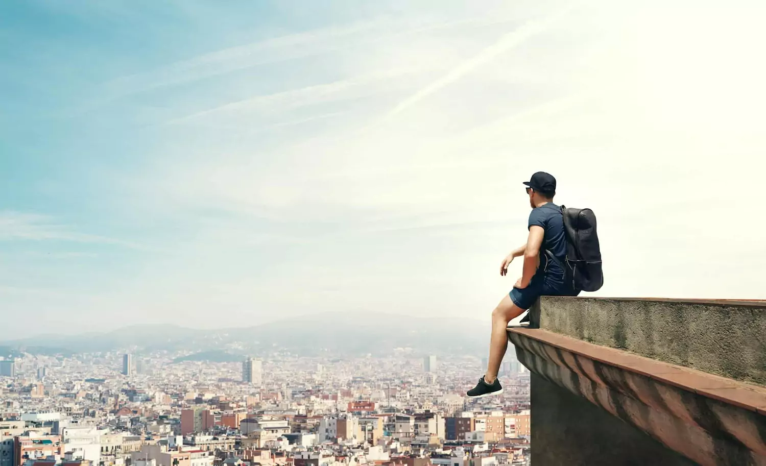 A man struggling with pornography sits on the edge of a tall building looking out across a city.