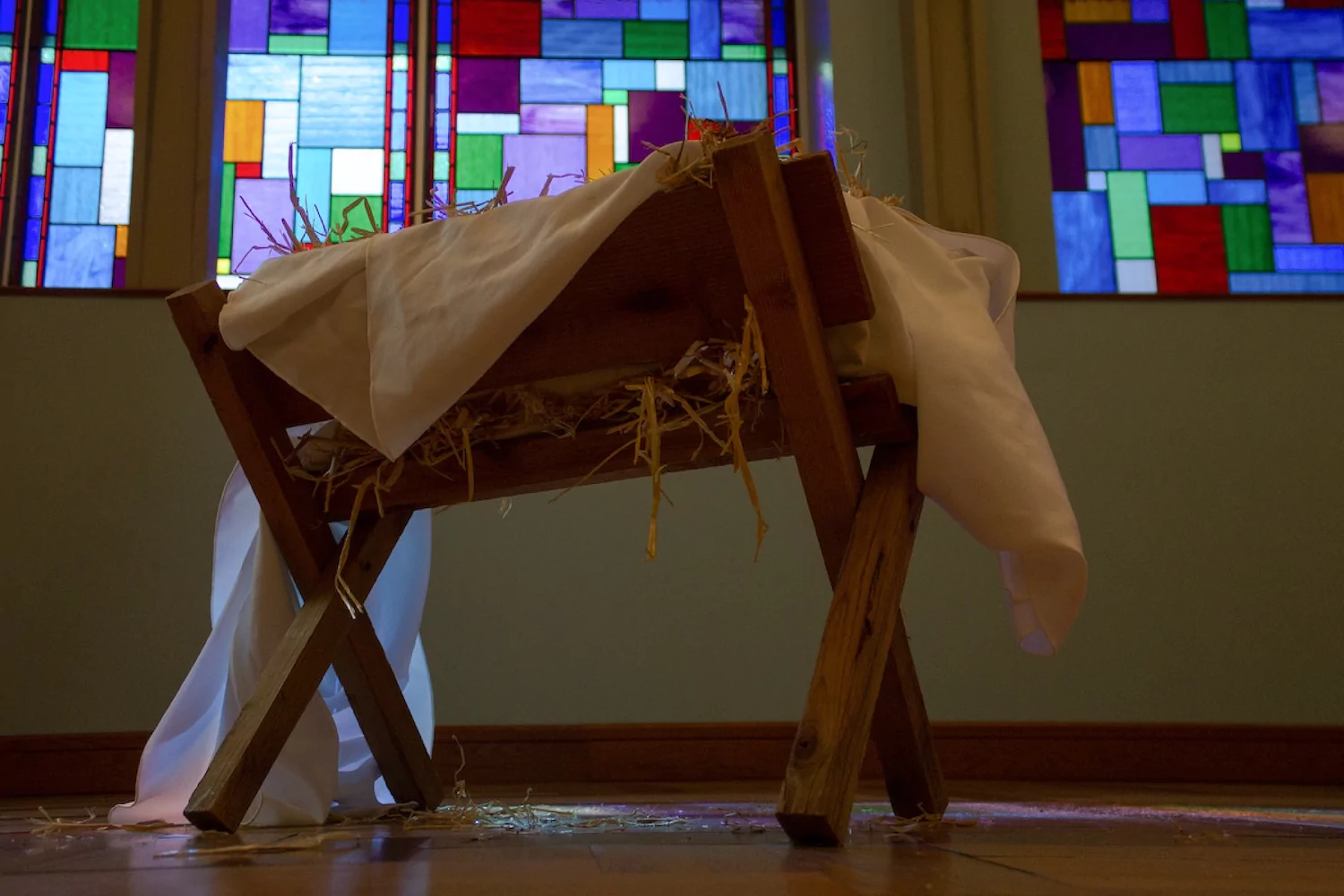 A manger sits in front of a church's stained glass window as a reminder of the incarnation.