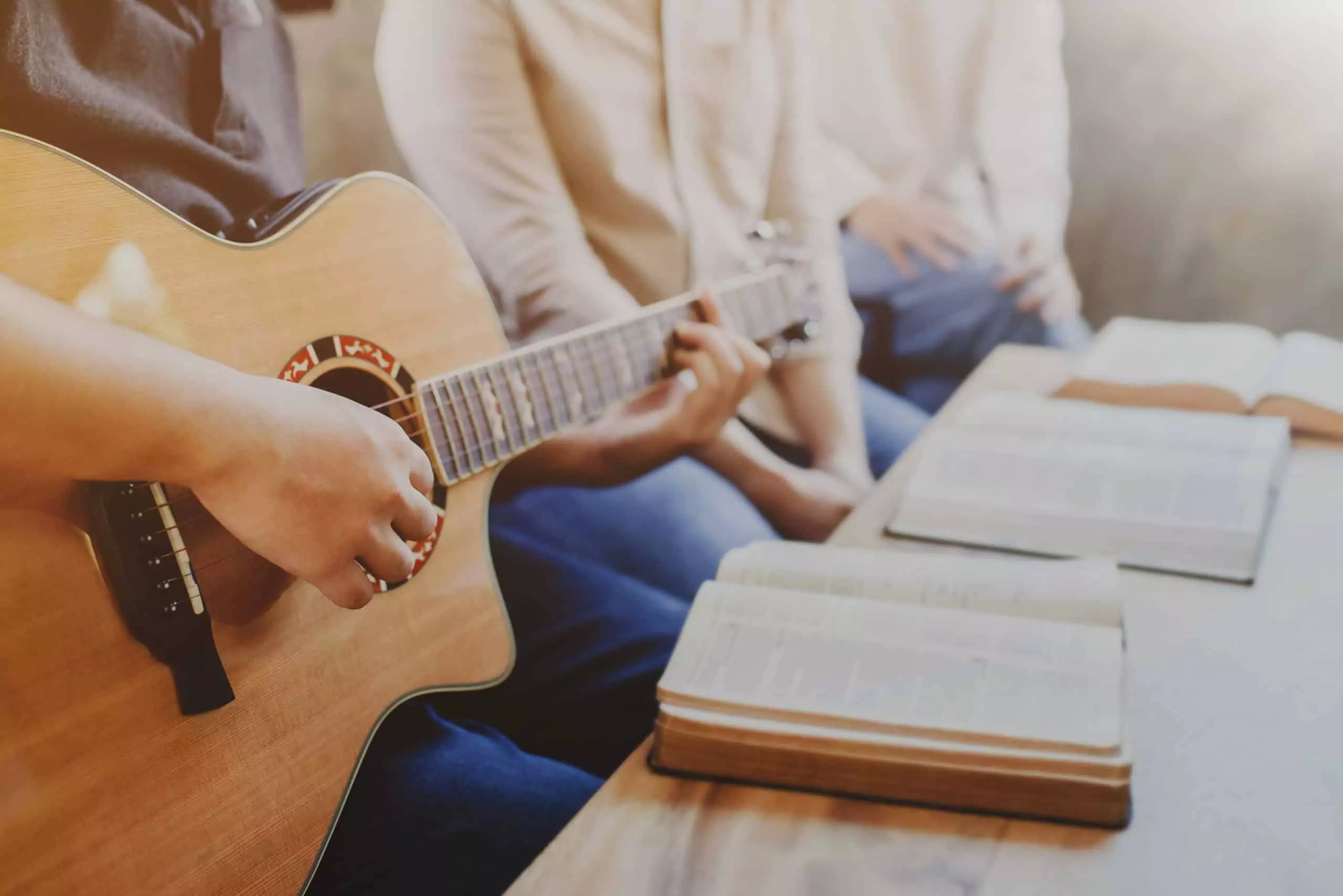 Church members sit around a coffee table with Bibles open as one man plays his guitar for worship.