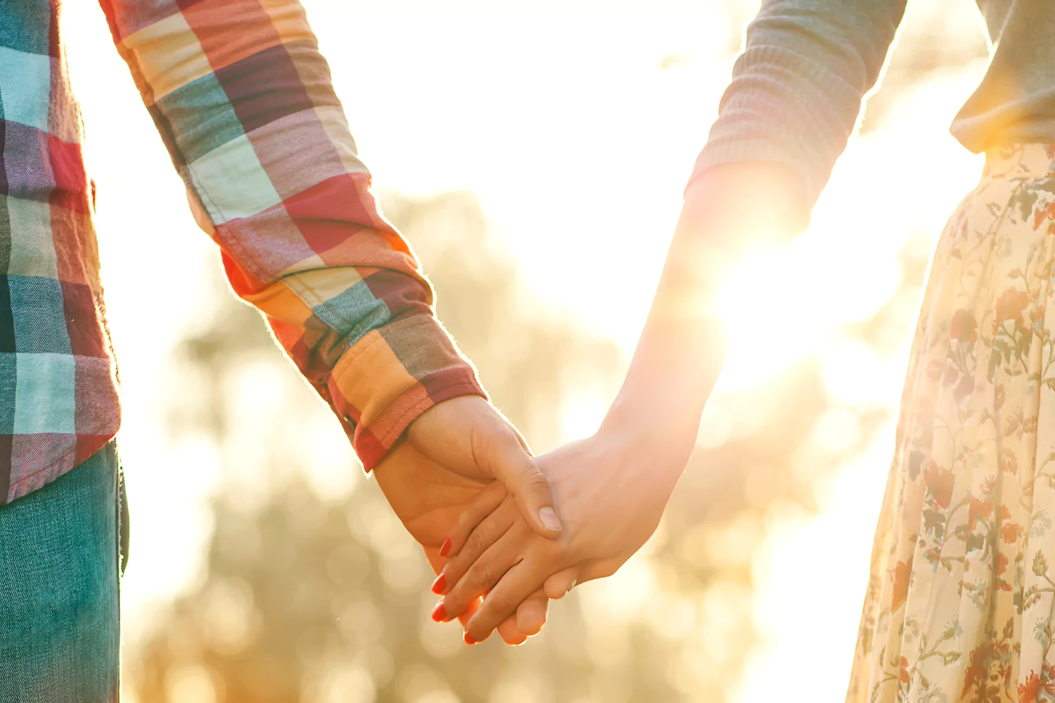 Close-up of a couple holding hands in the sunlight, representing connection, love, and the importance of a couples retreat.